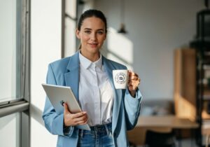 Stylish professional in a light blue blazer holding a tablet and Baden Bower mug, illustrating a media-ready image for EB-1A publicity.